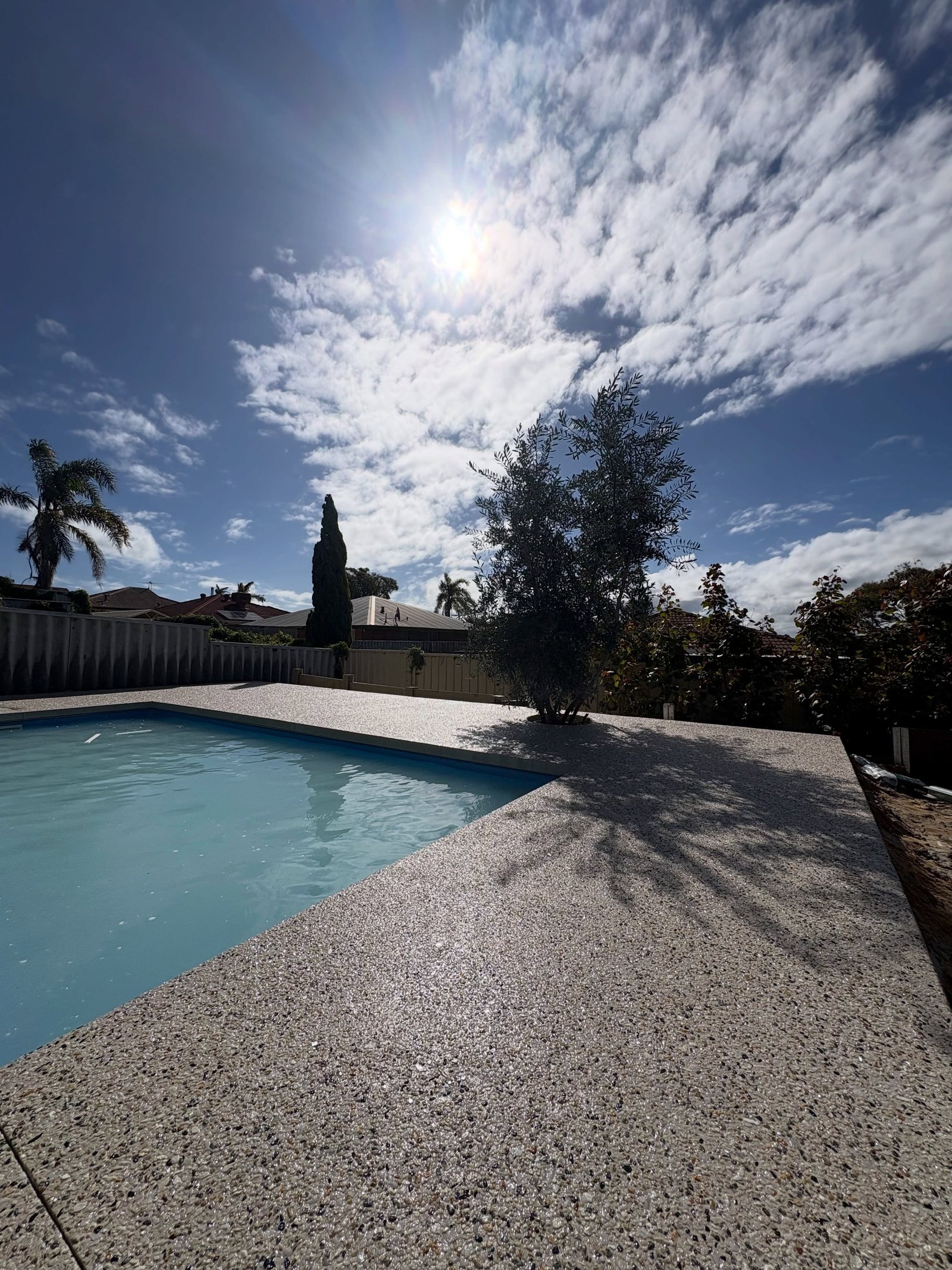 Exposed aggregate pool deck poured by CJH Concrete, sealed stone wrapping a backyard pool, August 2026